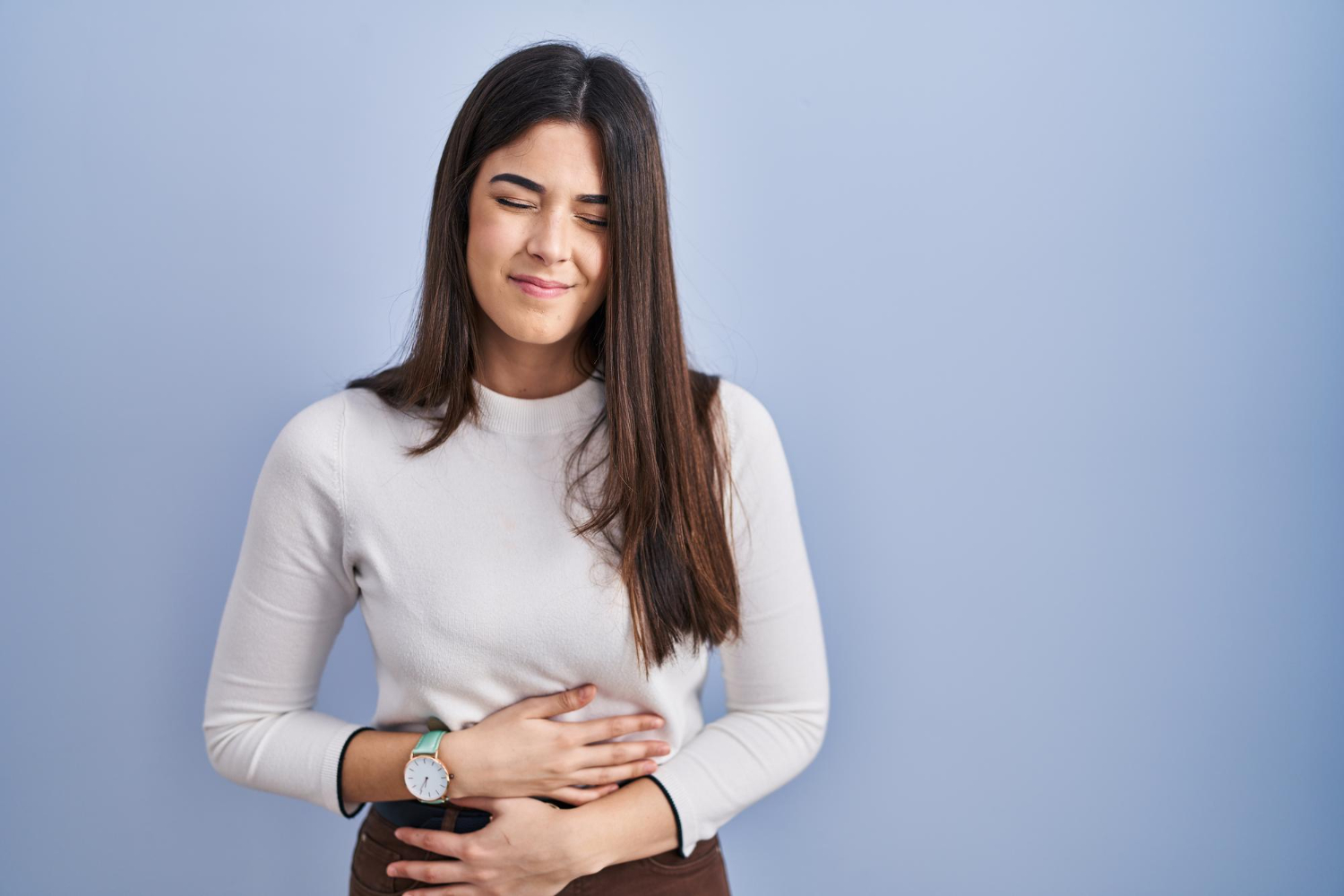 Mulher com a mão na barriga e cara de dor devido aos sintomas da adenomiose