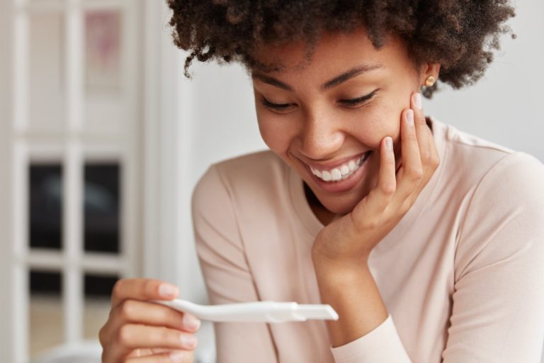Mulher feliz olhando o teste de gravidez após seguir as dicas para quem está tentando engravidar.