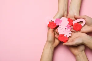 Mãos femininas seguram um modelo de útero de papel decorado com flores rosas e vermelhas, simbolizando o cuidado com a saúde uterina e a fertilidade. Ilustra a discussão sobre mioma no útero e a possibilidade de engravidar.