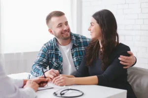 Casal sorridente em consulta médica sobre tratamento para engravidar na Clínica Huntington, recebendo orientação para reprodução assistida.