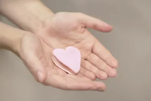 Mãos em concha segurando um coração rosa, simbolizando o óvulo doado e o processo de ovodoação.