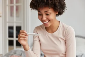 Mulher negra sorridente segurando um teste de gravidez, simbolizando a esperança e as possibilidades da fertilidade feminina.