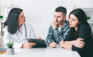 Médica em consultório conversa com casal visivelmente preocupado sobre as opções de tratamento de infertilidade.