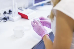 Mãos de uma profissional com luvas rosas manuseando um pequeno objeto em laboratório, exemplificando a meticulosidade necessária no processo de como congelar óvulos.