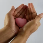 Mãos delicadamente segurando um coração rosa, simbolizando o ato de dar e o processo de como doar óvulos no Brasil.