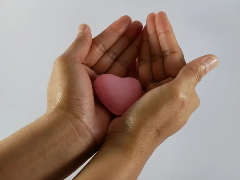 Mãos delicadamente segurando um coração rosa, simbolizando o ato de dar e o processo de como doar óvulos no Brasil.