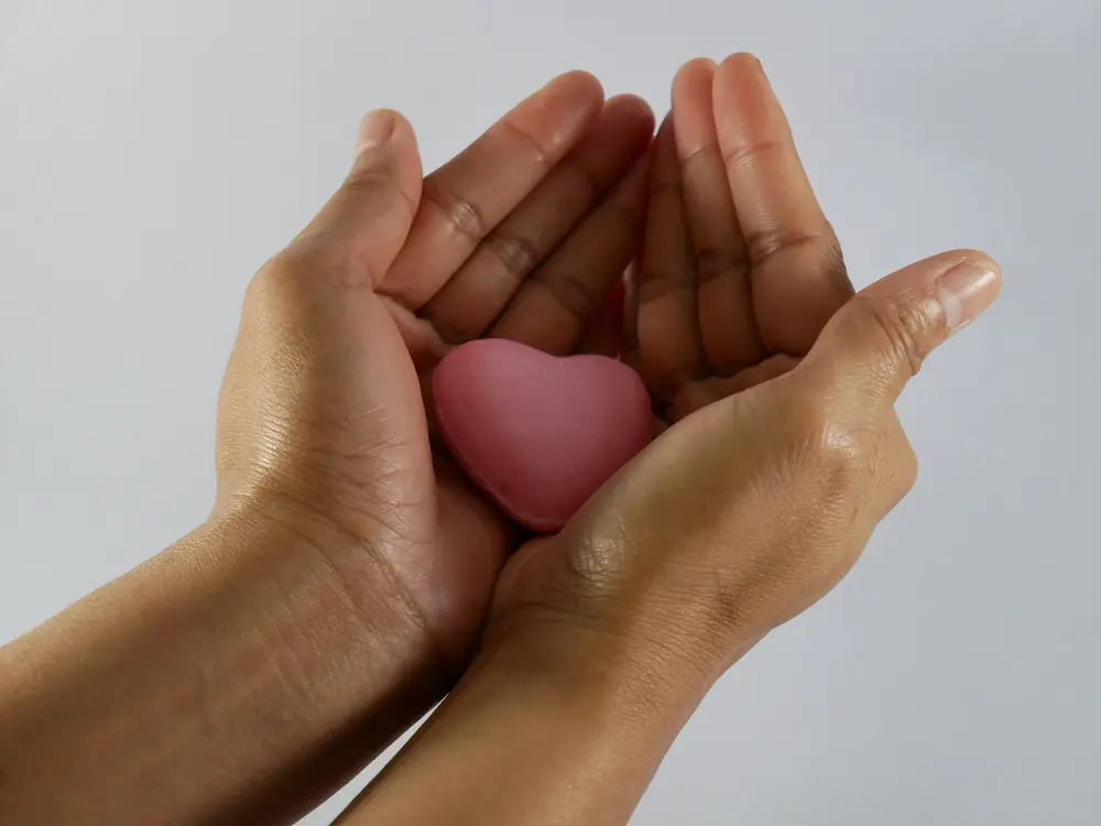 Mãos delicadamente segurando um coração rosa, simbolizando o ato de dar e o processo de como doar óvulos no Brasil.