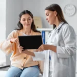 Médica em consultório explicando o processo de indução da ovulação a uma paciente, utilizando um tablet para apresentar informações e dados relevantes.
