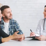 Casal sorridente em consulta com médica, recebendo informações sobre técnicas de reprodução assistida para ajudar a engravidar.