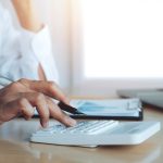 Mulher com calculadora, caneta e papel em cima da mesa, calculando quanto custa uma inseminação artificial