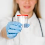 Enfermeira de luvas mostrando o coletor usado na doação de sêmen.