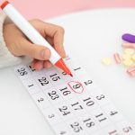 Mão feminina circulando os dias da janela fértil no calendário.