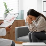 Médica explicando o que causa aborto espontâneo à uma paciente com as mãos em frente ao rosto.