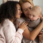 Casal homoafetivo de duas mulheres com um filho biológico no colo.