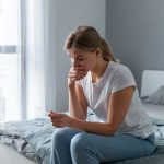 Mulher sentada na cama, segurando um teste de gravidez, refletindo sobre a perda gestacional e quando tentar novamente.