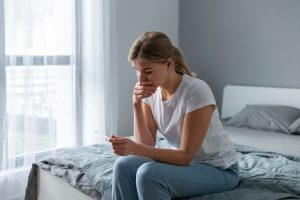 Mulher sentada na cama, segurando um teste de gravidez, refletindo sobre a perda gestacional e quando tentar novamente.
