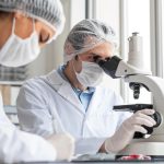 Especialistas em embriologia analisando amostras em laboratório de reprodução assistida com auxílio de microscópio.