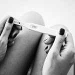 Foto em preto e branco de duas mãos segurando um teste de gravidez negativo após a FIV.