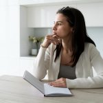 Mulher sentada à mesa, com um caderno nas mãos pensando se deve optar pela criopreservação de óvulos.