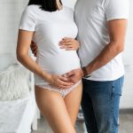 Casal abraçado segurando a barriga da mulher que optou pela gravidez por FIV, que não é considerada de risco.
