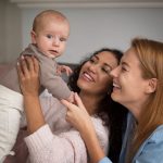 Duas mulheres segurando e sorrindo para um bebê que foi gerado a partir de uma inseminação artificial com duas mães.