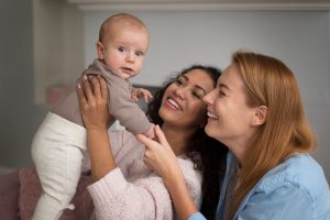 Duas mulheres segurando e sorrindo para um bebê que foi gerado a partir de uma inseminação artificial com duas mães.