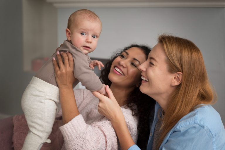 Duas mulheres segurando e sorrindo para um bebê que foi gerado a partir de uma inseminação artificial com duas mães.