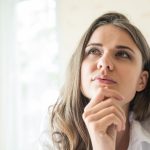 Mulher com a mão no queixo pensando se a Fertilização In Vitro dói ou não.