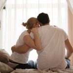 Casal de costas sentado abraçado e triste pensando nas principais causas da infertilidade.