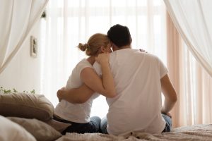 Casal de costas sentado abraçado e triste pensando nas principais causas da infertilidade.