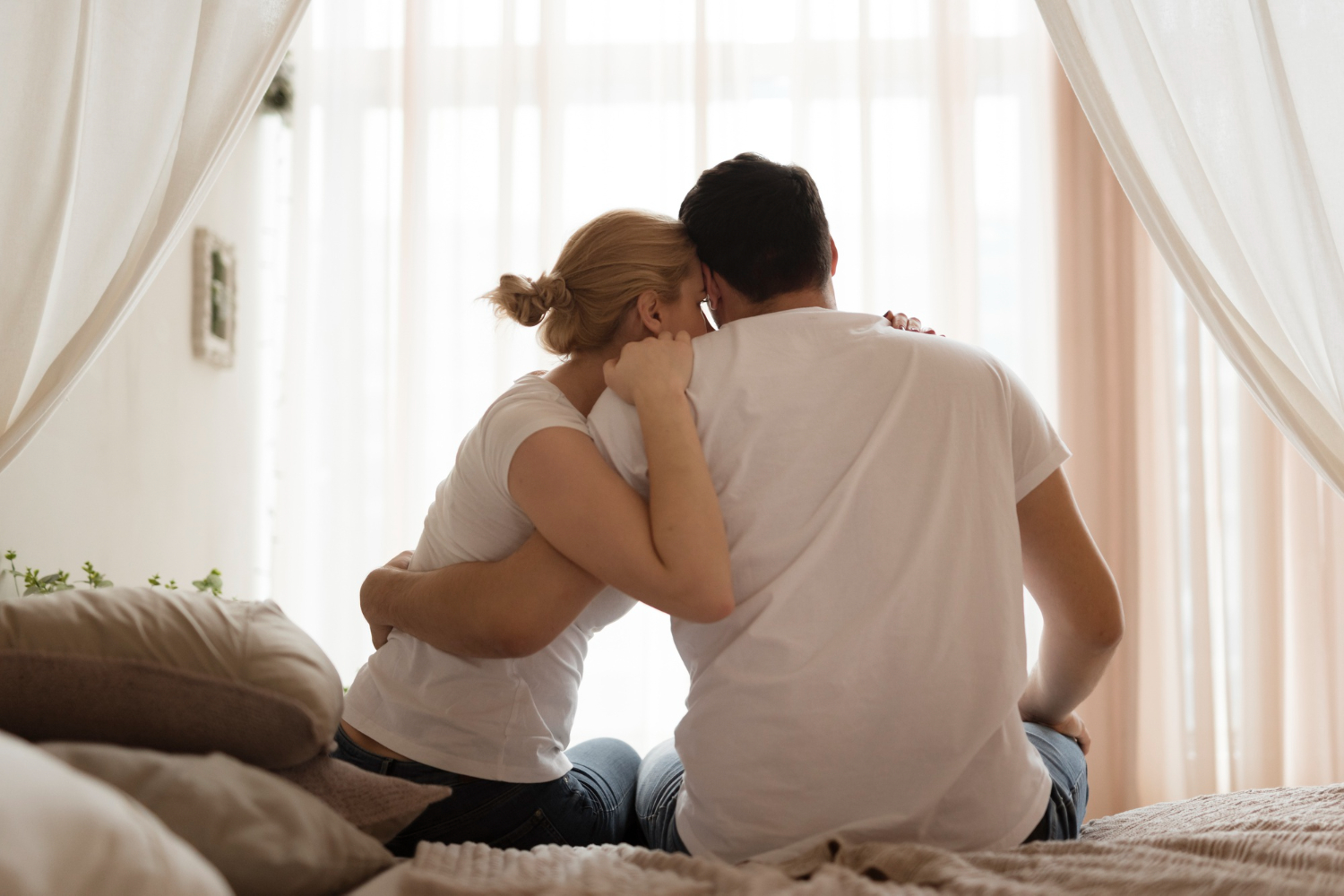 Casal de costas sentado abraçado e triste pensando nas principais causas da infertilidade.
