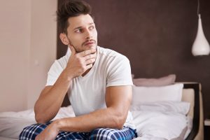 Jovem sentado com a mão no queixo refletindo sobre o relógio biológico do homem e como afeta a fertilidade