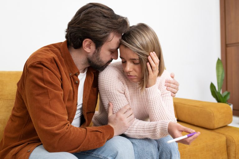 Casal infértil abraçado com um exame de gravidez na mão.