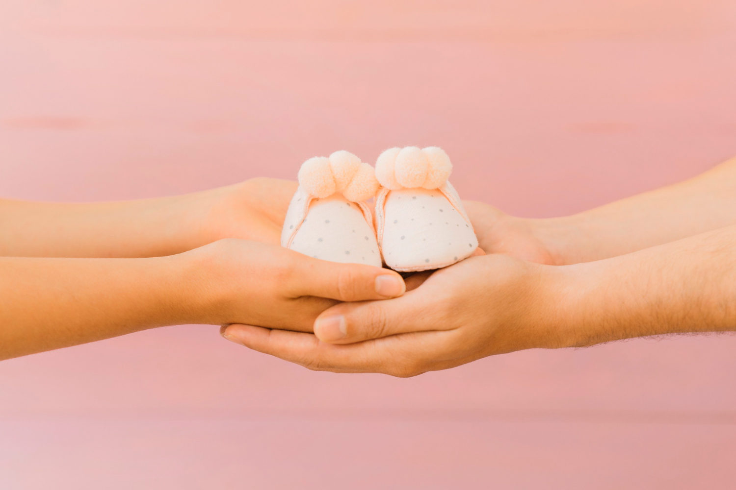 Mãos de uma mulher passando sapatinhos de bebê para outra, simbolizando a doação de embriões.