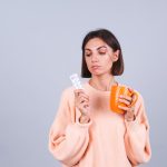 Mulher segurando comprimidos e uma xícara com água se perguntando para que serve o estradiol na FIV