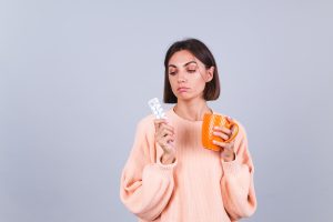 Mulher segurando comprimidos e uma xícara com água se perguntando para que serve o estradiol na FIV