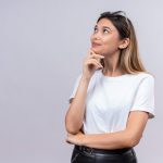 Mulher jovem com a mão no queixo de perguntando se congelamento de óvulos tem efeitos colaterais