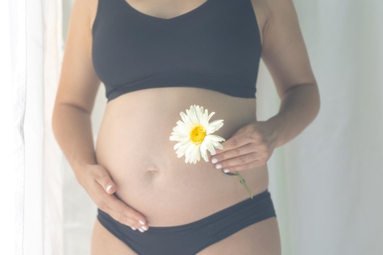 Mulher grávida segurando a barriga e uma flor após recorrer à gravidez por ovorecepção.