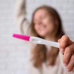 Mulher feliz segurando o teste de gravidez positivo apó9s seguir os passos para conseguir engravidar