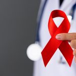 Médico segurando o laço vermelho que representa a conscientização sobre ISTs para falar de fertilidade.