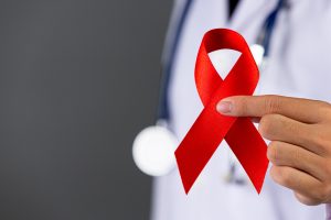 Médico segurando o laço vermelho que representa a conscientização sobre ISTs para falar de fertilidade.