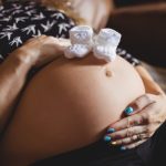 Mulher grávida com sapatinhos na barriga após passar por FIV em ciclo natural