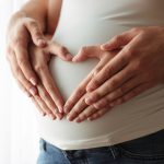 Casal fazendo um coração na barriga da mulher após fazer o Beta hCG quantitativo