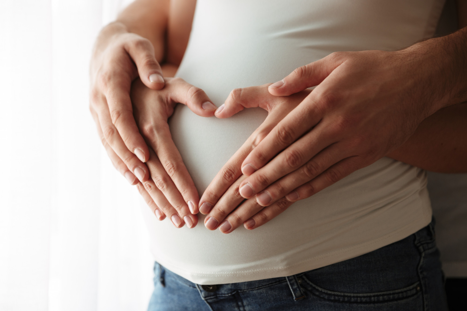Casal fazendo um coração na barriga da mulher após fazer o Beta hCG quantitativo