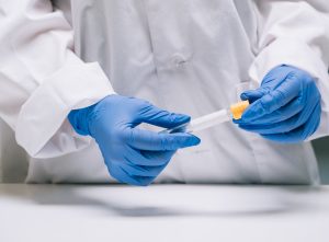 Mãos de um profissional com um tubo de coleta para que o paciente possa repetir o espermograma