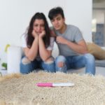 Casal que não consegue engravidar olhando triste para o teste de gravidez.