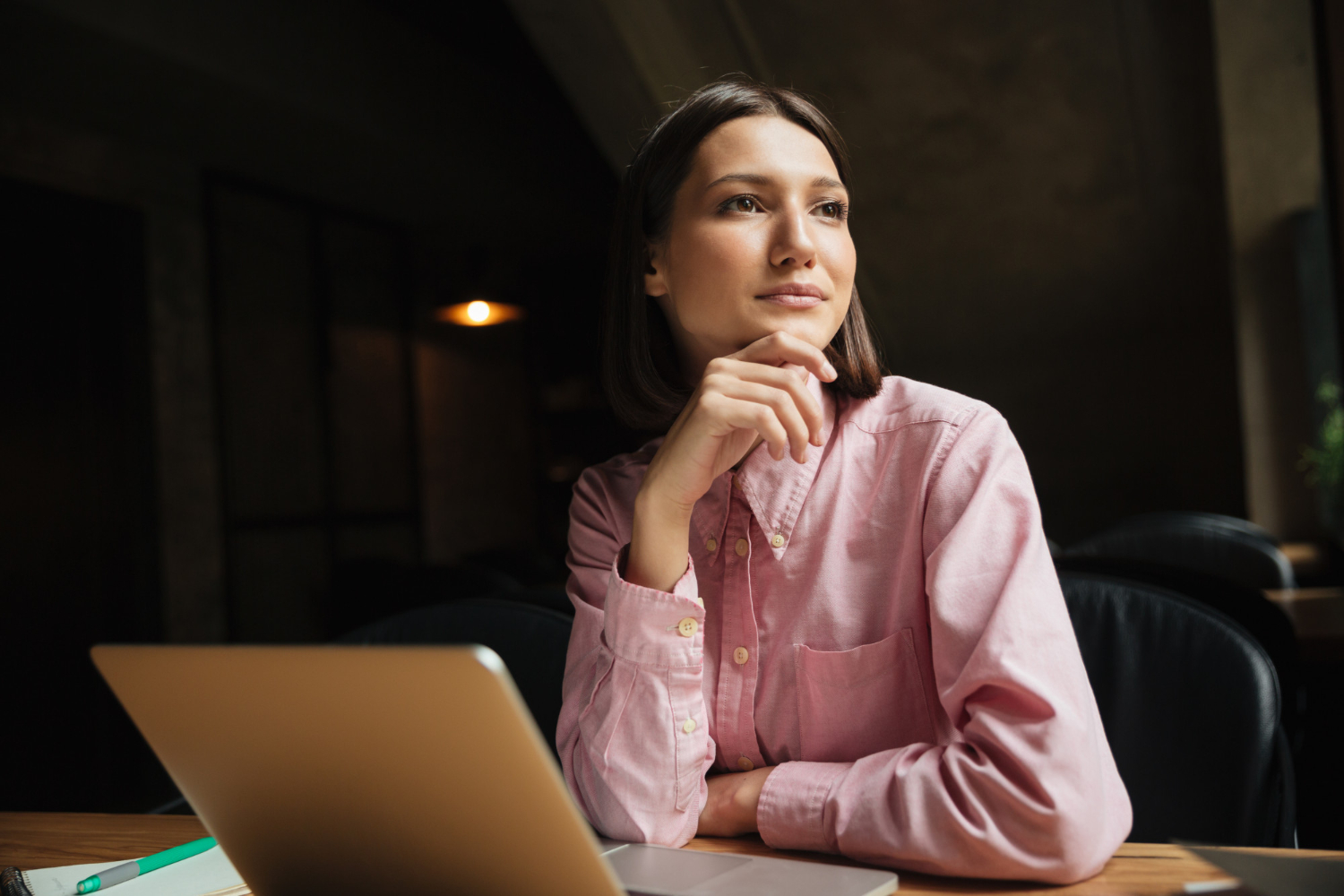 Mulher com a mão no queixo pensando "como saber se sou fértil?" em frente a um notebook para pesquisar sobre especialistas em fertilidade.